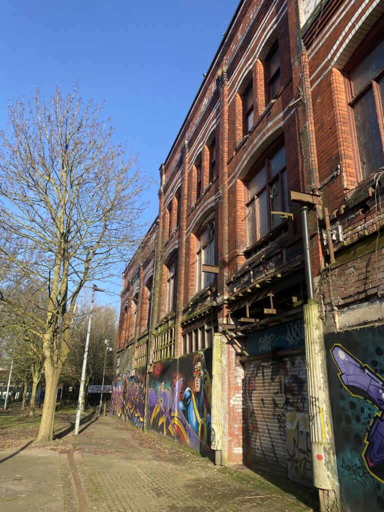 Left side of the front of Hulme Hippodrome on a sunny day, showing graffiti and broken windows