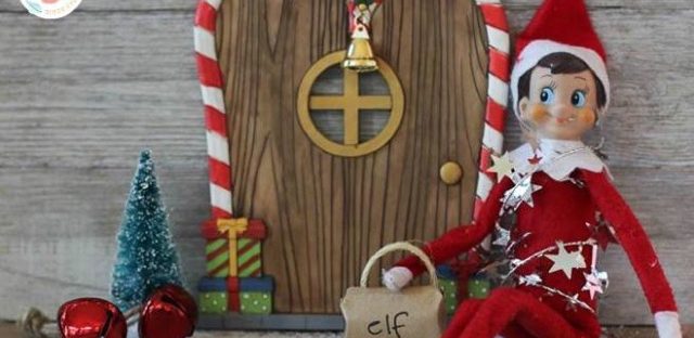 Elf on The Shelf doll sitting in front of a gingerbread house style door
