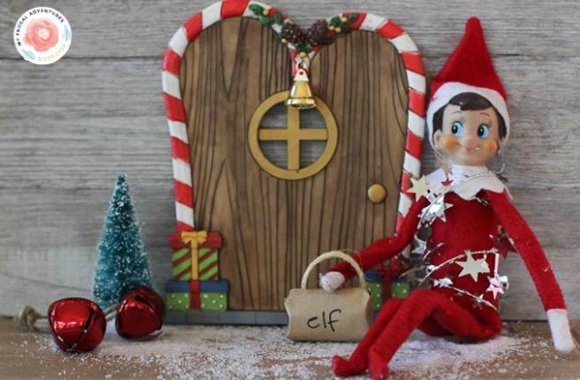 Elf on The Shelf doll sitting in front of a gingerbread house style door