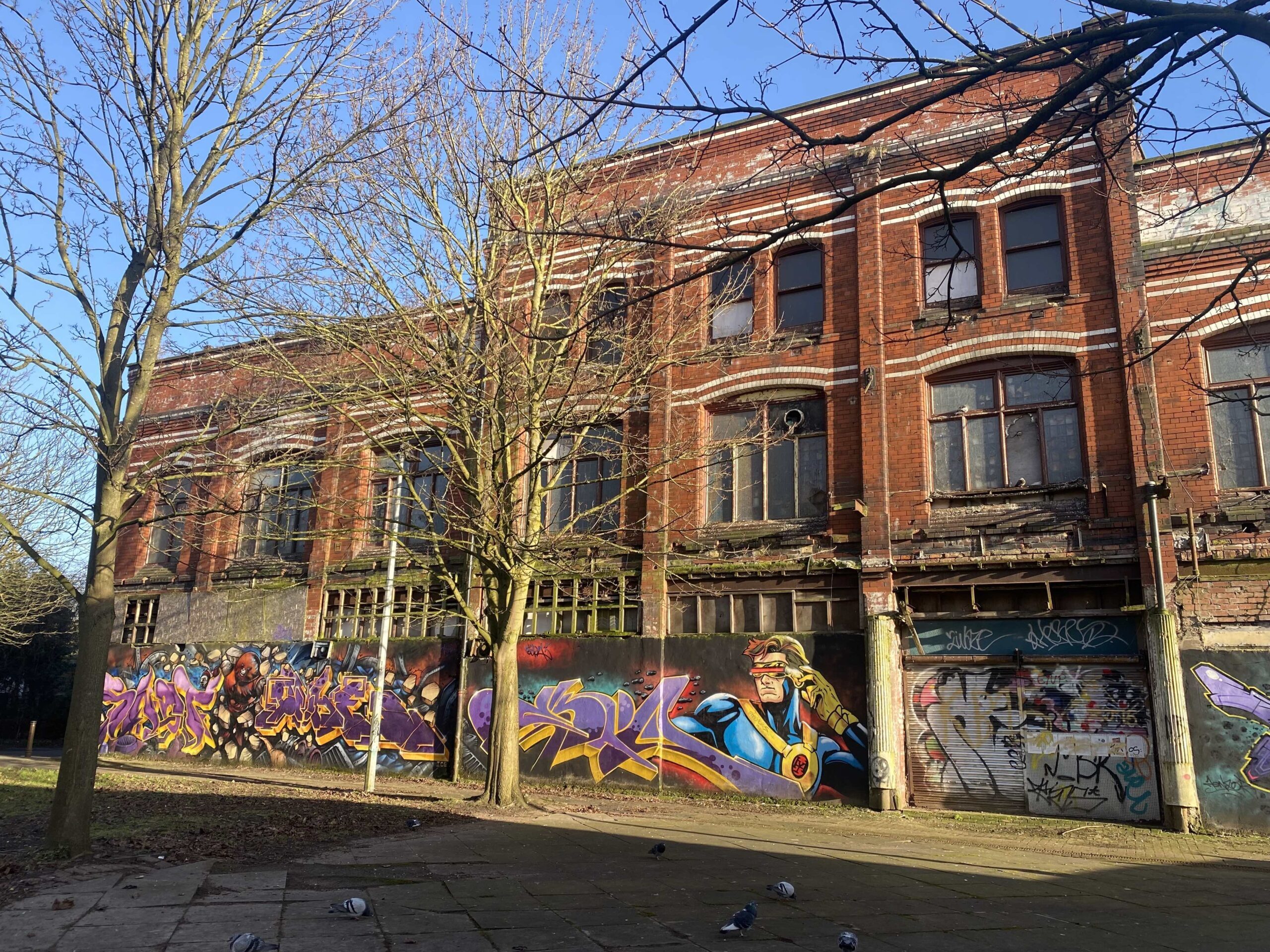 Graffitied and neglected front side of Hulme Hippodrome, with trees in front, on a sunny day