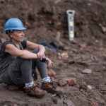 Linda Brogan sat on a brick in a builders hat at excavation of the Reno surrounded by rubble