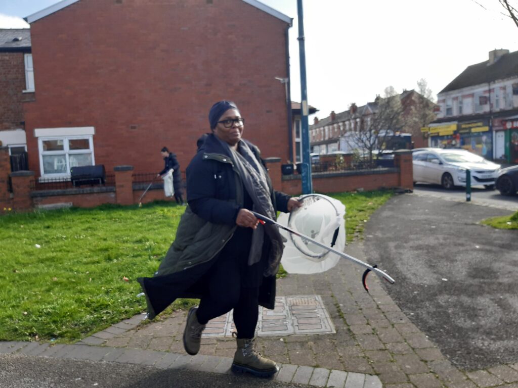 Woman with bag and litter picker on street picking up rubbish. 