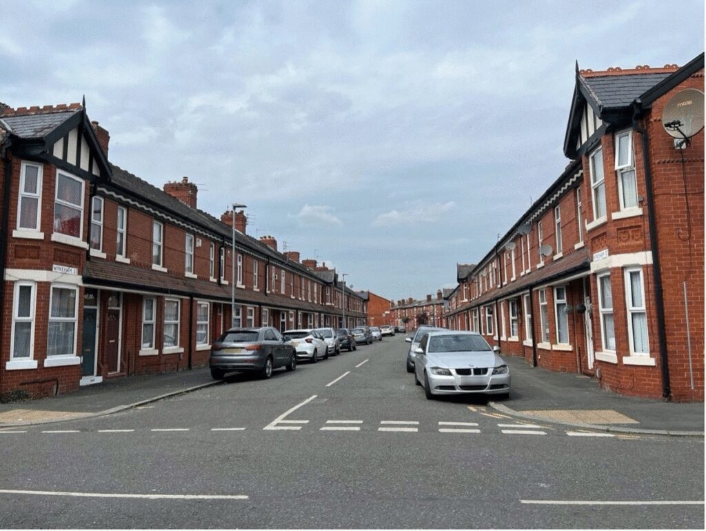 Two rows of housing on Maine Road with cars parked outside.