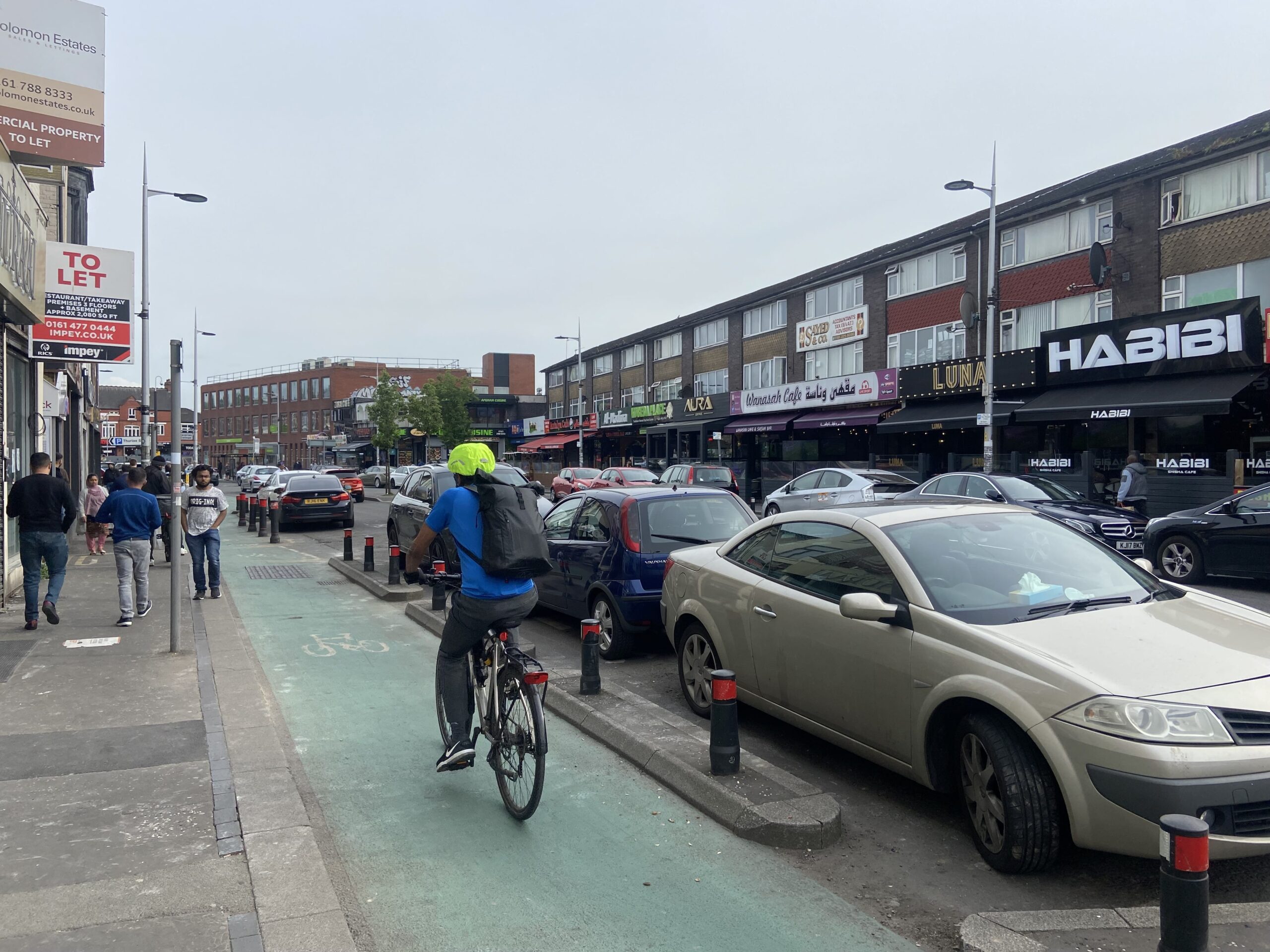 A photograph of cars parked along with curry mile with a cyclist using the cycle lane.