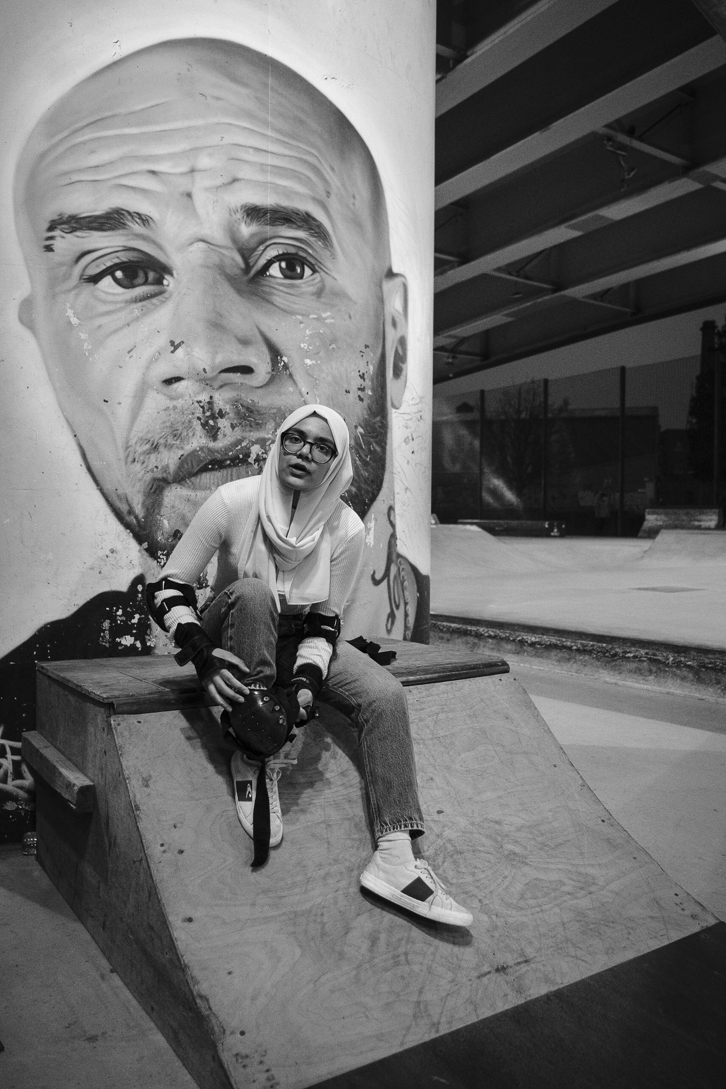 A woman sitting down holding a skateboard with a large image of a man behind her.