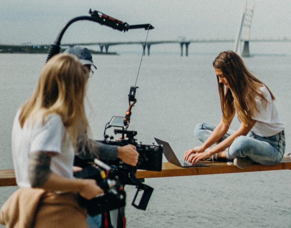 Woman taking a picture of another woman sitting on the bench near a river