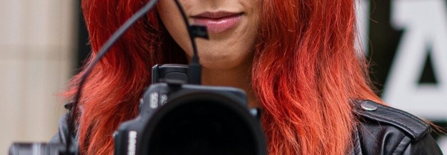 Woman director holding camera- wearing black leather jacket with bright red hair