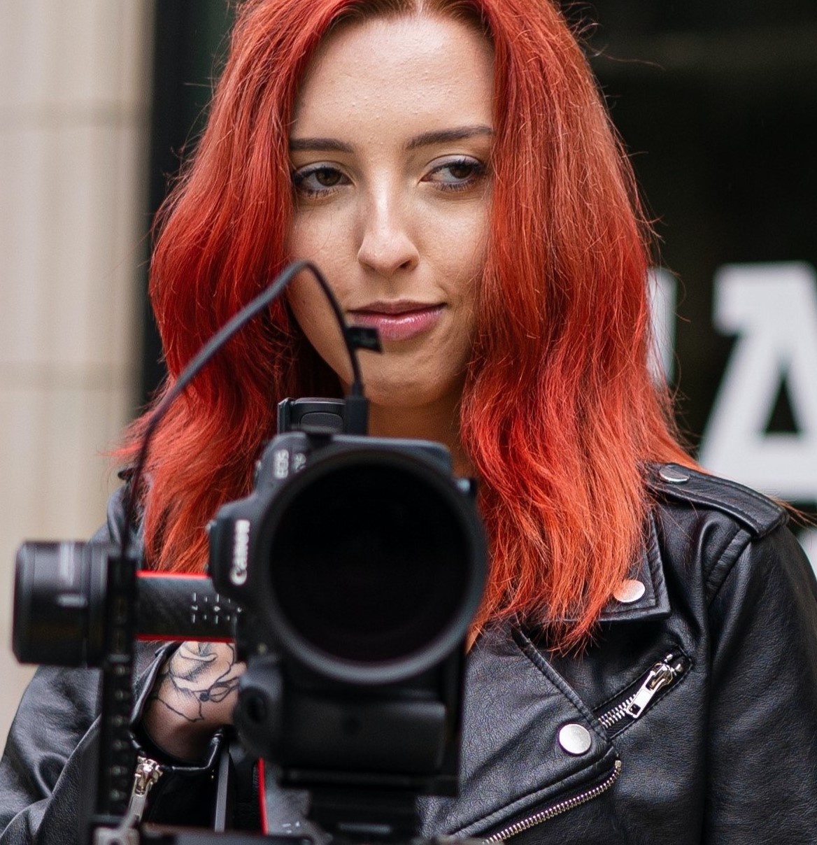 Woman director holding camera- wearing black leather jacket with bright red hair