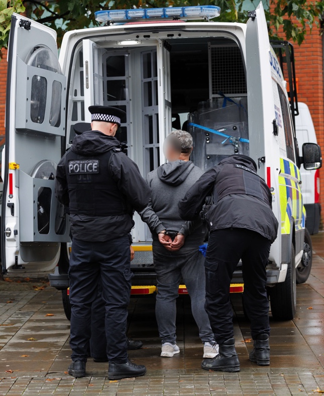 two police officers arresting a man infront of police van