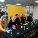 Mayoral candidates sitting at a table in the Manchester Evening News offices. From left to right: Hannah Spencer, Laura Evans, Andy Burnham, Dan Barker, and Jake Austin. Each candidate has a notebook, a mug, and a bottle of water. There is a yellow backdrop with the Manchester Evening News logo.