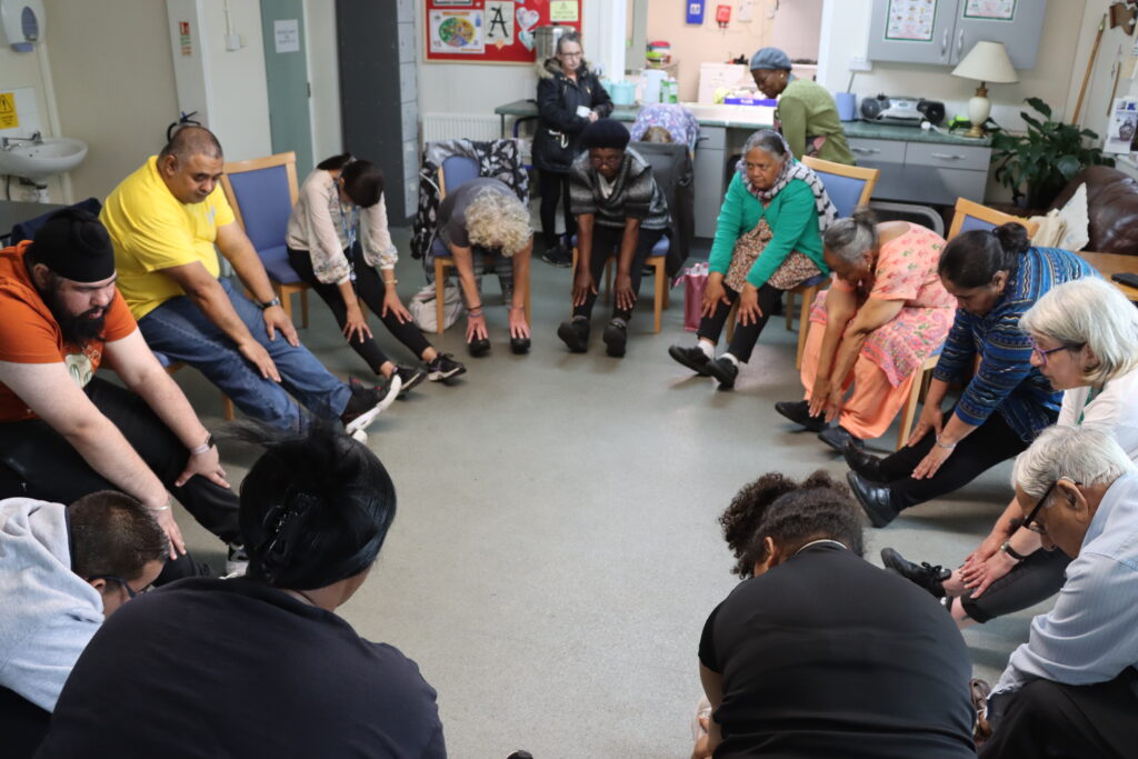 A group of people sit in chairs, touching feet, stretching as part of Empower 8 class.