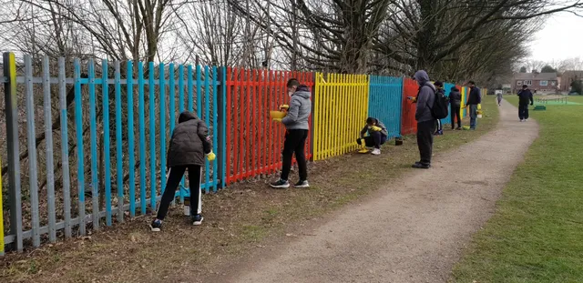 Children painting a fence in colours along a park.
