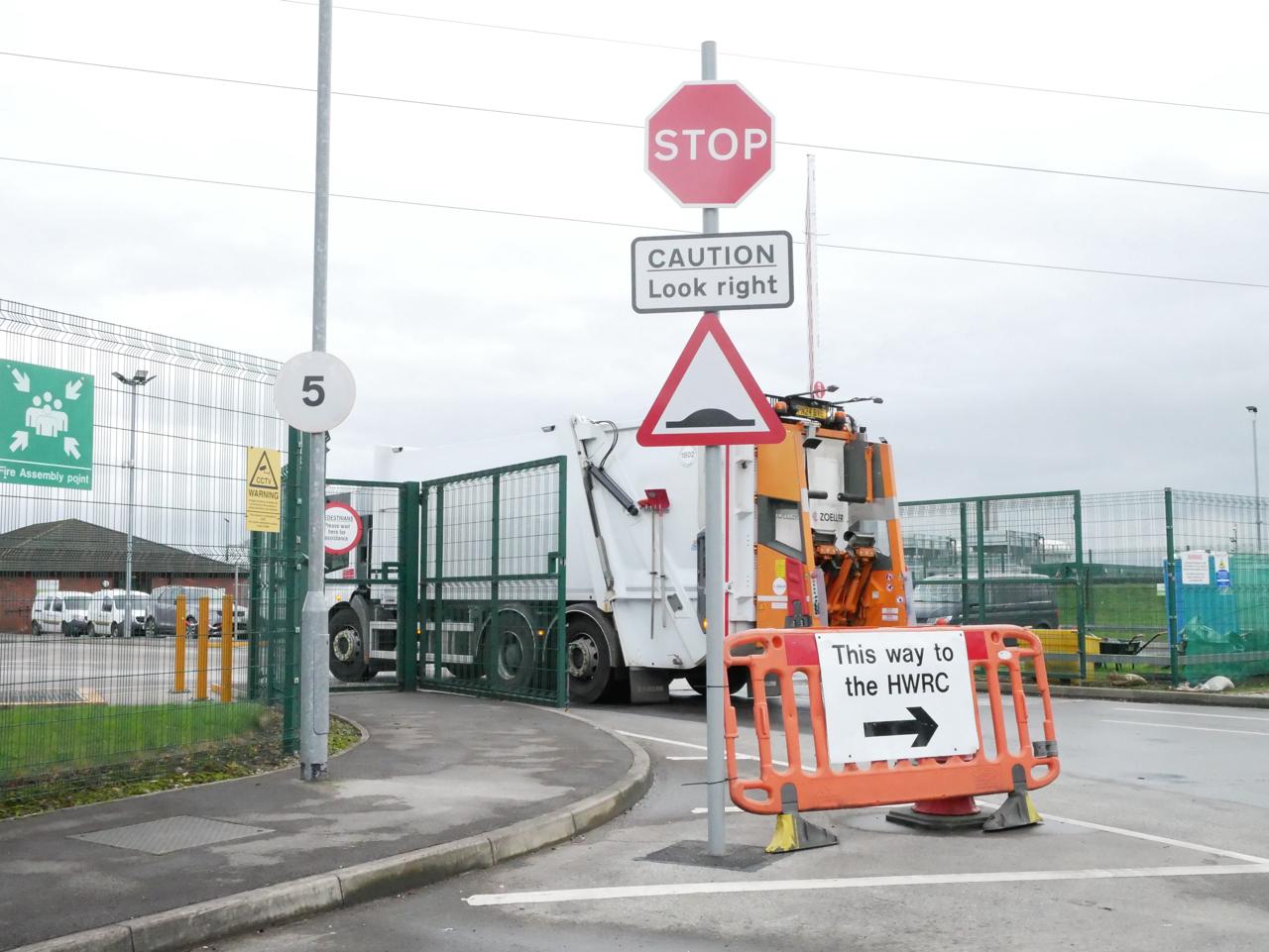 Exterior gates of Bolton recycling facility. A bin lorry is moving forward past a sign that reads "This way to the HWRC"