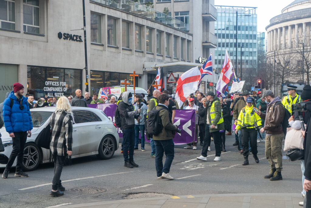 UKIP protesters march down Oxford Road through St. Peter's Squuare holding UKIP banners and English flags. Some are wearing high-vis jackets.