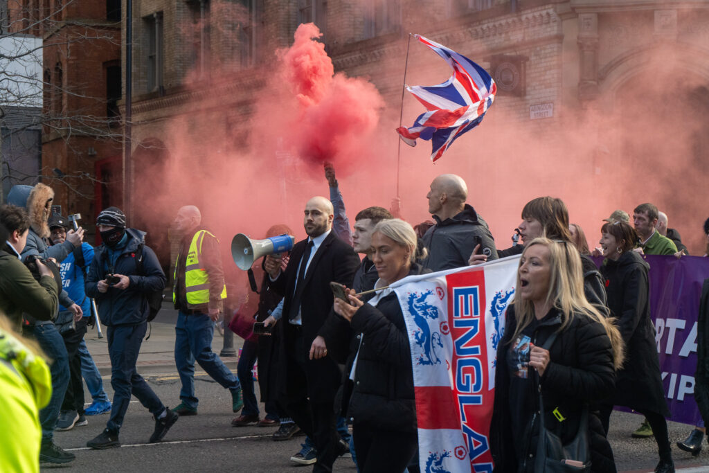 UKIP protesters set off red smoke flares and hold English flags. Nick Tenconi is at the front of the crowd holding a megaphone. 