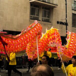 A red Chinese dragon puppet being paraded above a crowd by a team of puppeteers.