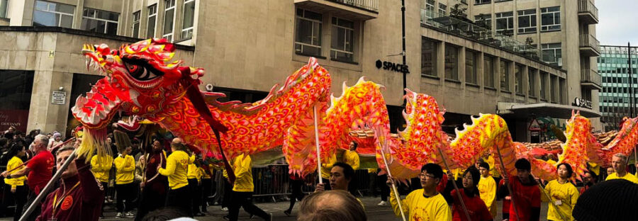 A red Chinese dragon puppet being paraded above a crowd by a team of puppeteers.