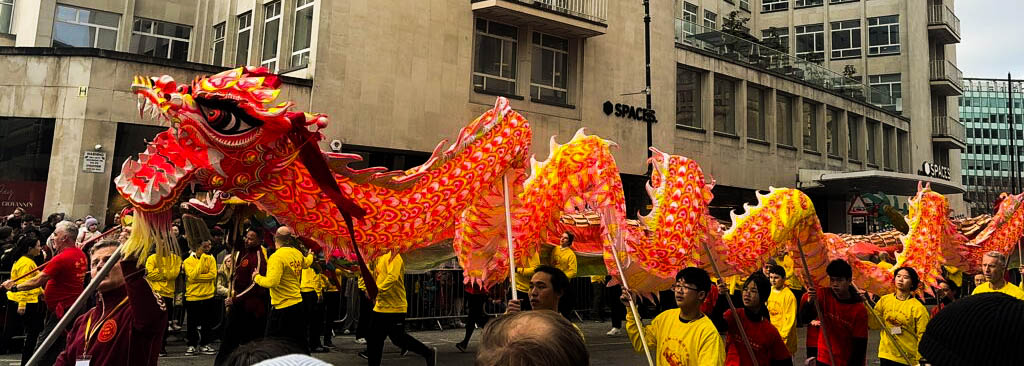 A red Chinese dragon puppet being paraded above a crowd by a team of puppeteers.