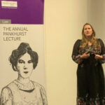 Laura Bates, a white woman with blonde hair wearing a long black dress, is mid-speech. She is standing next to a large sign on the left of the image which reads “The annual Pankhurst lecture” with a pen illustration of Emmeline Pankhurst underneath.