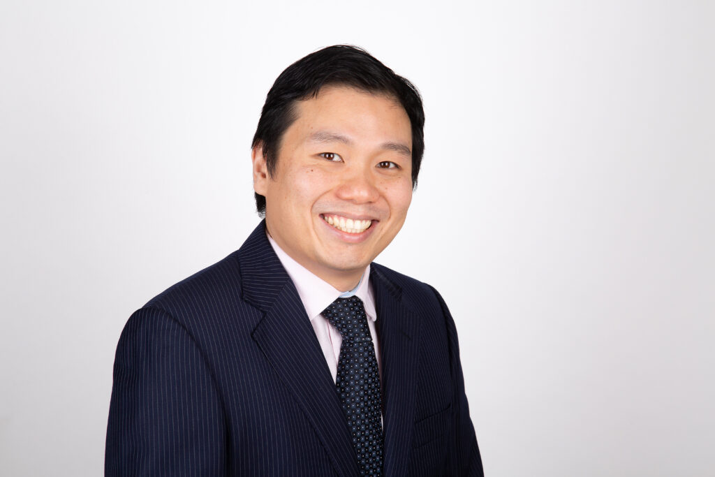 Dr. Kenneth Ma, an East-Asian man with short hair, smiles into the camera. He is wearing a dark suit and tie, and here is a blank white background