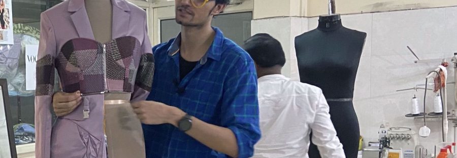 An Indian man in a blue shirt and bright yellow glasses stands next to a mannequin displaying a modular outfit