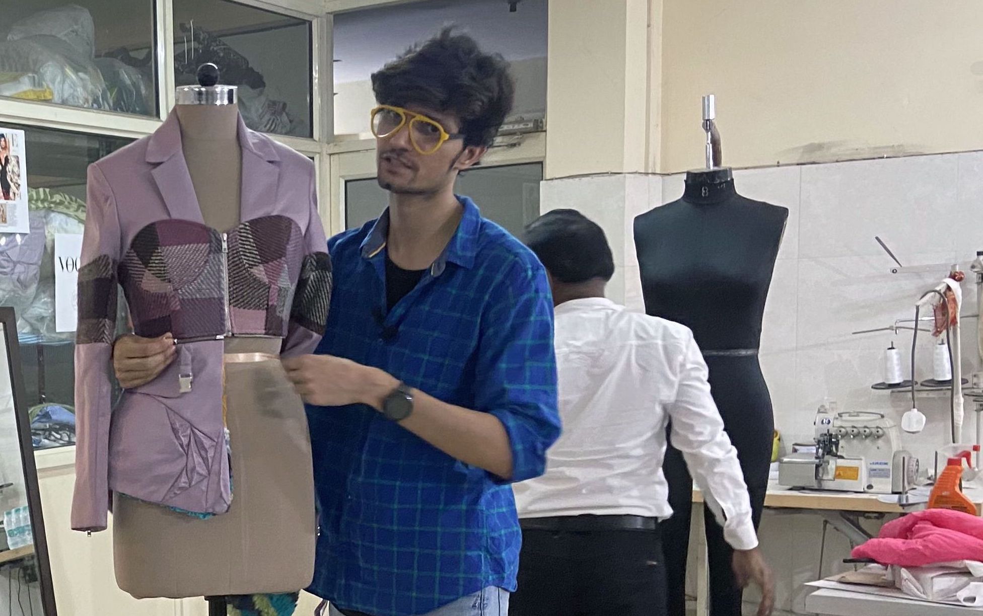 An Indian man in a blue shirt and bright yellow glasses stands next to a mannequin displaying a modular outfit