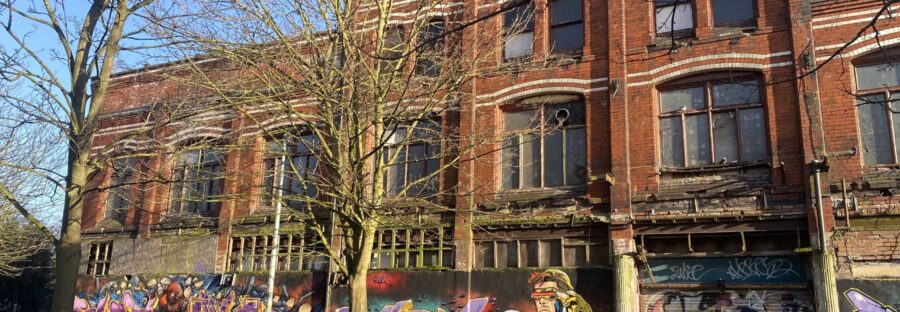 Graffitied and neglected front side of Hulme Hippodrome, with trees in front, on a sunny day