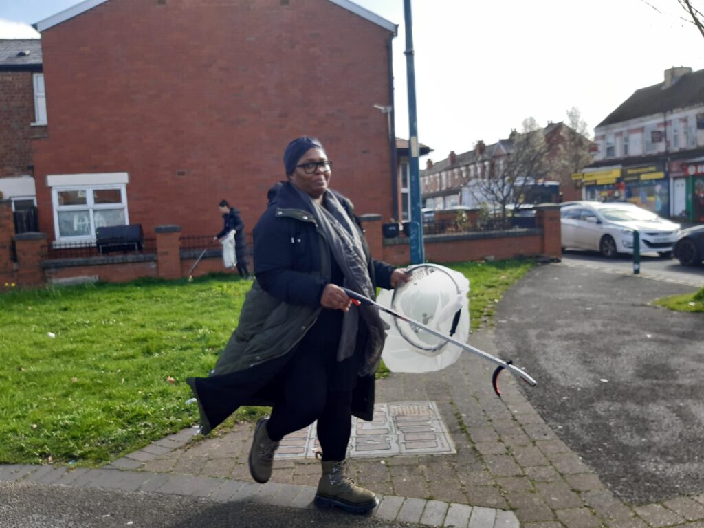 Woman with bag and litter picker on street picking up rubbish.