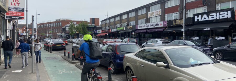 A photograph of cars parked along with curry mile with a cyclist using the cycle lane.