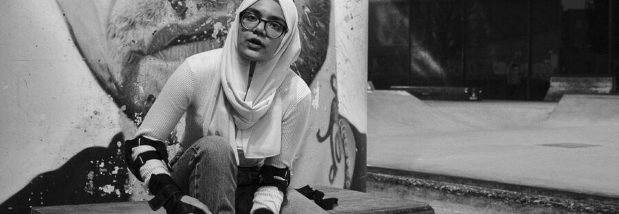 A woman sitting down holding a skateboard with a large image of a man behind her.