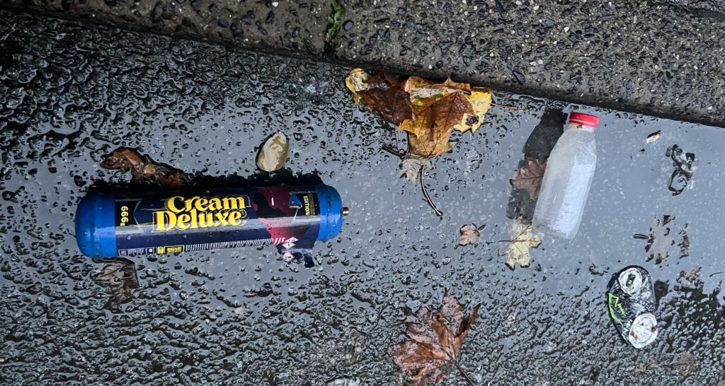 'Nos' Canister discarded with other litter on Manchester street.