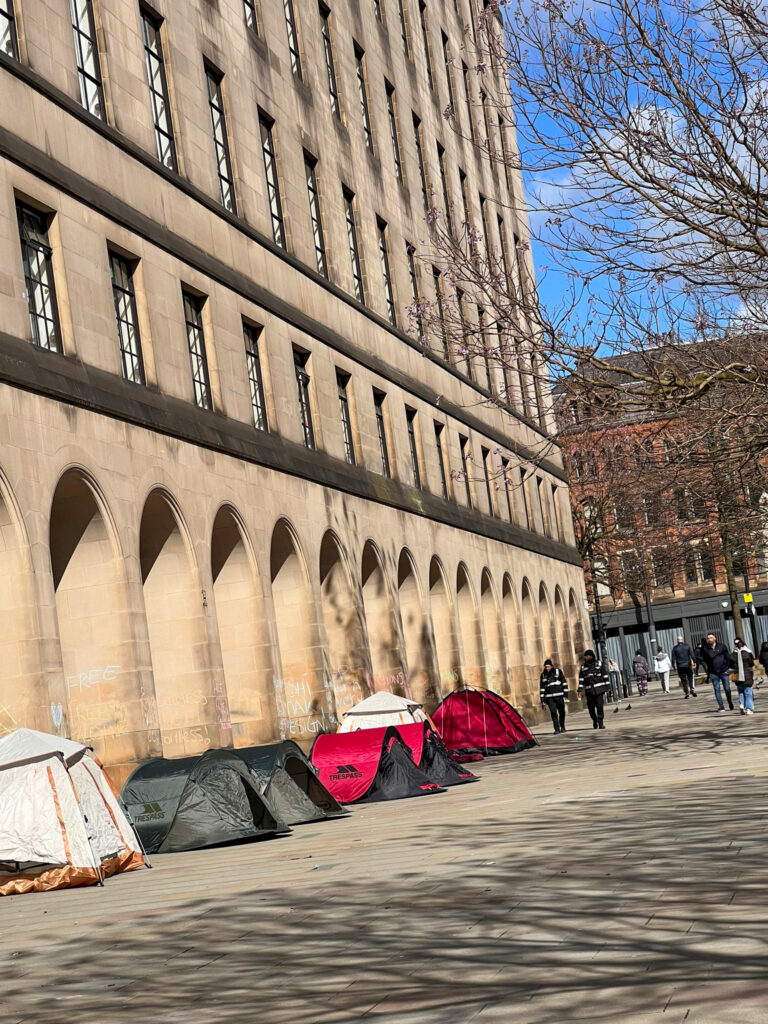 Four tents in St. Peter's Square, Manchester with support messages for a ceasefire chalked on the wall.