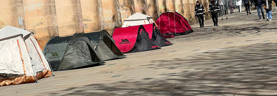 Four tents in St. Peter's Square, Manchester with support messages for a ceasefire chalked on the wall.