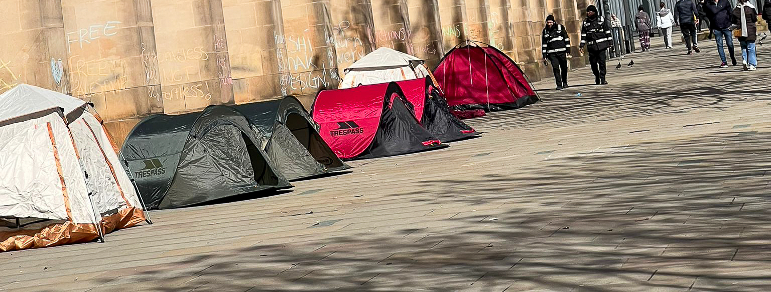 Four tents in St. Peter's Square, Manchester with support messages for a ceasefire chalked on the wall.