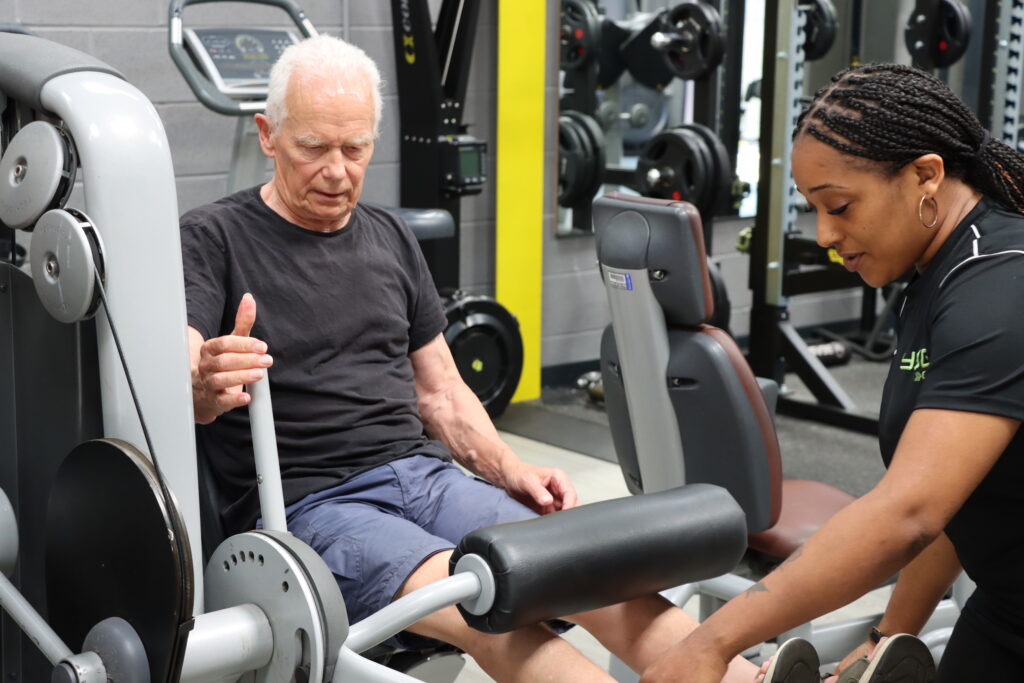 A man using gym equipment for quads with help of female instructor.