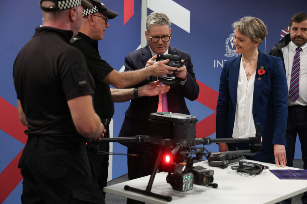 Prime Minister Sir Keir Starmer and Home Secretary Yvette Cooper attending the Interpol General Assembly in November. Starmer is holding and inspecting a police drone handed to him by a representative of the police as Ms Cooper watches, smiling.