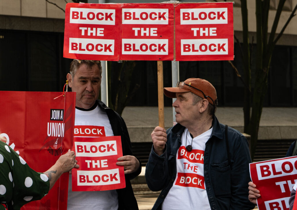 Two Block the Block protesters wear red and white T-Shirts and hold red-and-white signs, both of which say 'Block the Block'