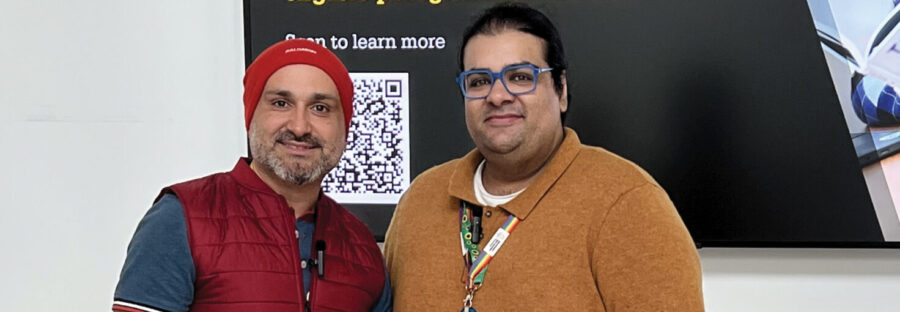 Faraz Arian (left) wears a red beanie and gilet over a blue shirt and grey ripped jeans. He is smiling at the camera and holding a sheet of paper. On the right of the image is Amraze Khan, who wears a yellow jumper and light jeans. He is also smiling into the camera.