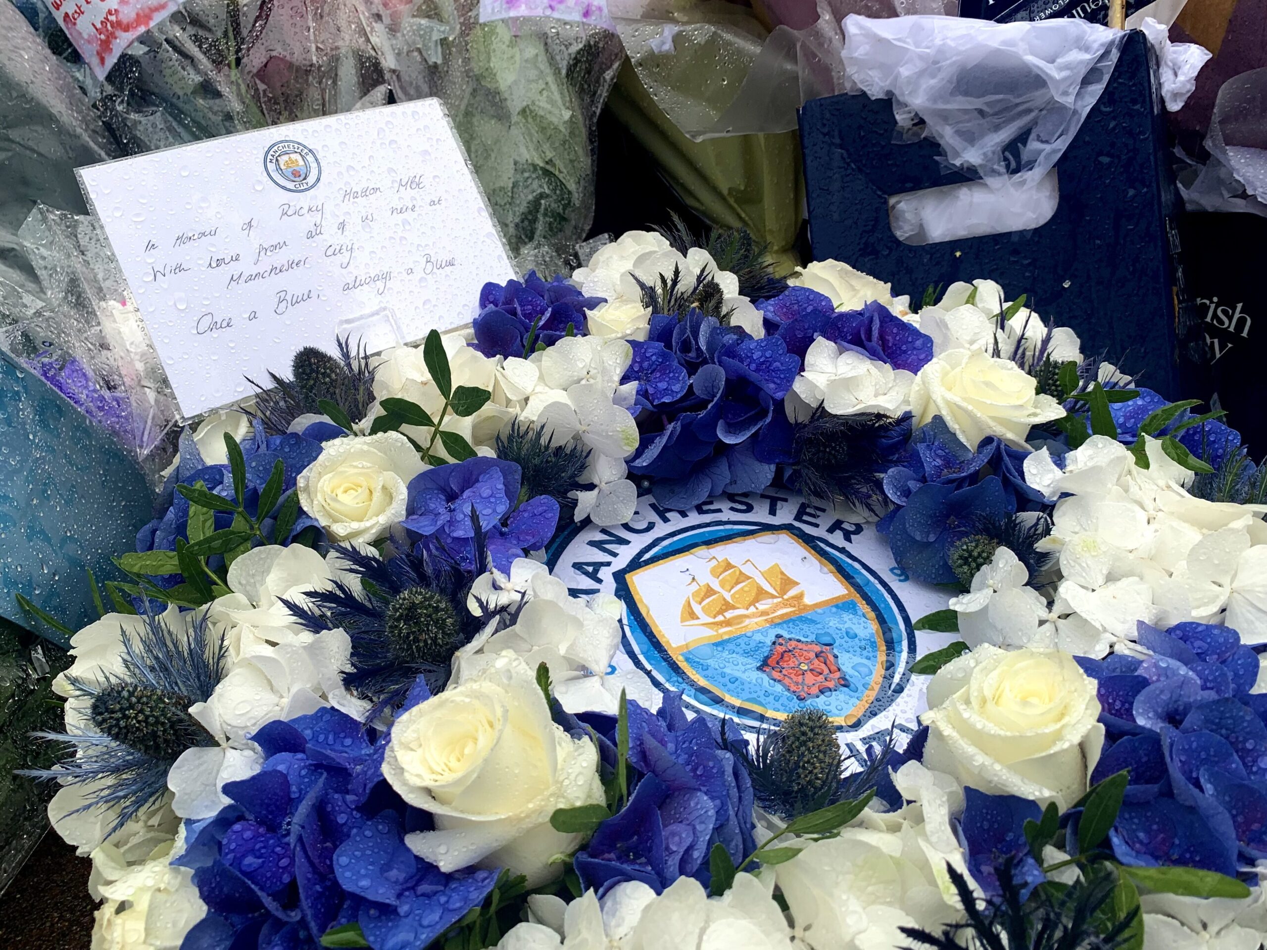 A wreath of blue and white flowers, with a Manchester City logo in the middle. A card sticks out of the top of the wreath. It reads: “In memory of Ricky Hatton MBE. With Love from all of us at Manchester City. Once a Blue, always a Blue.”