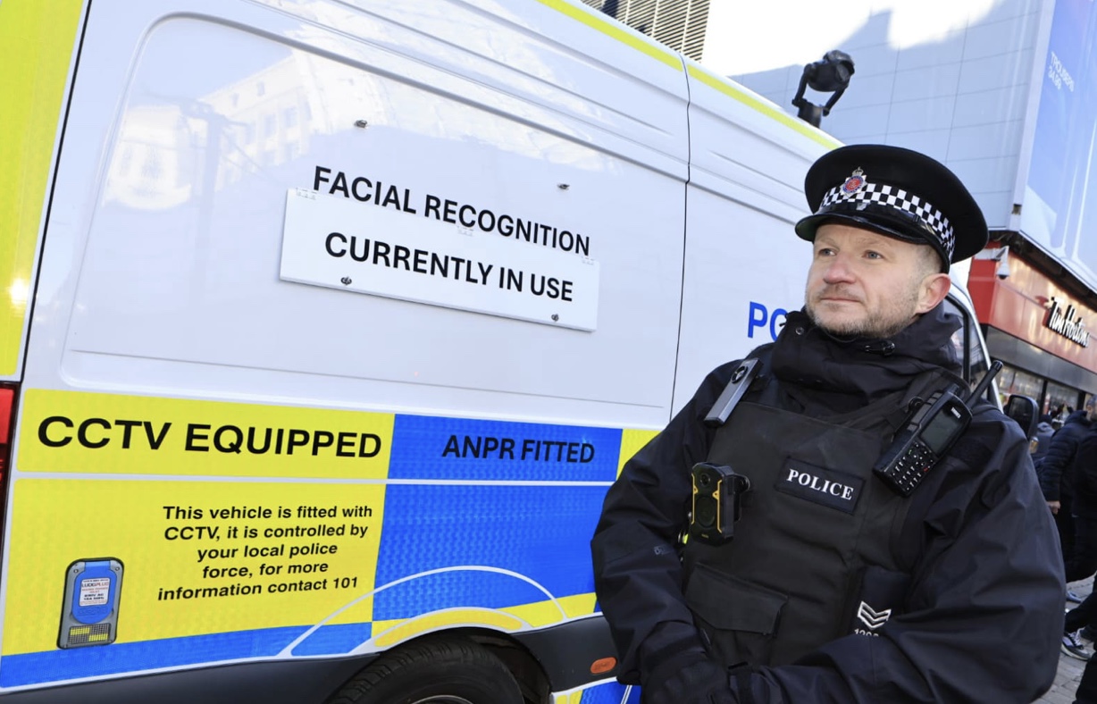 Photo of police officer stood in front of Live Facial Recognition police van.