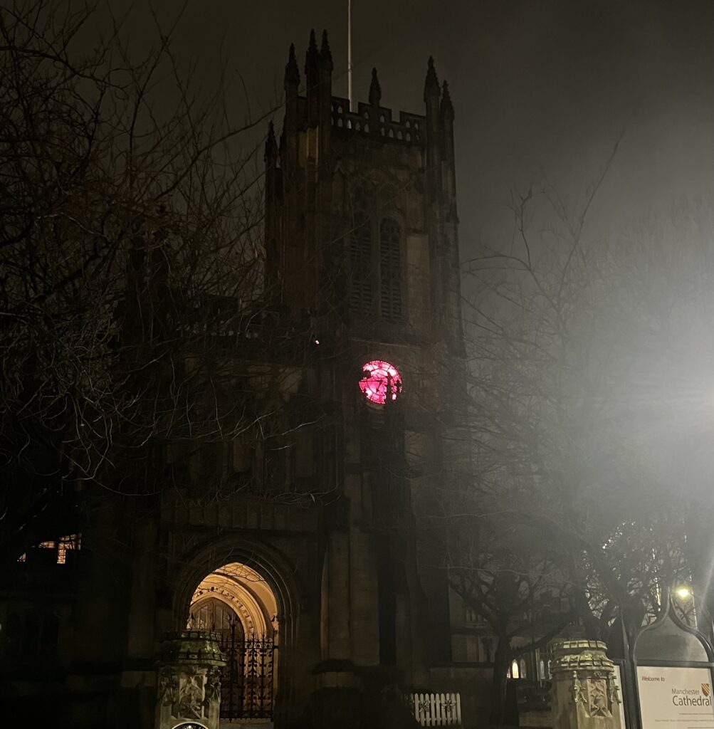 Picture of the clock at Manchester Cathedral lit up pink for Henshaws event.