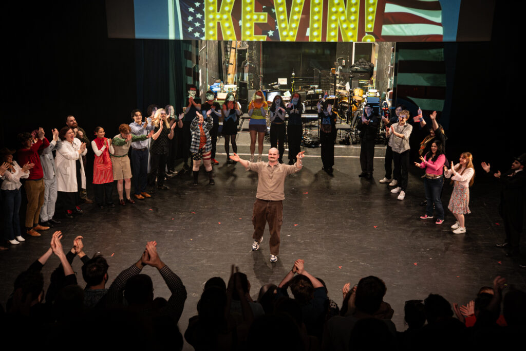 People stood in a circle on a stage clapping to a person in the middle